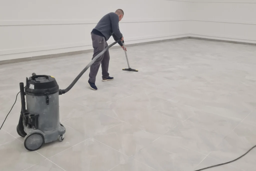 Radnik industrijskim usisivačem dubinski čisti keramički pod velikog magacina